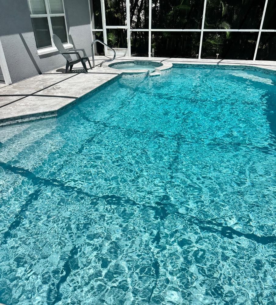 Clear blue pool with spa and glass tile, inside a screen enclosure